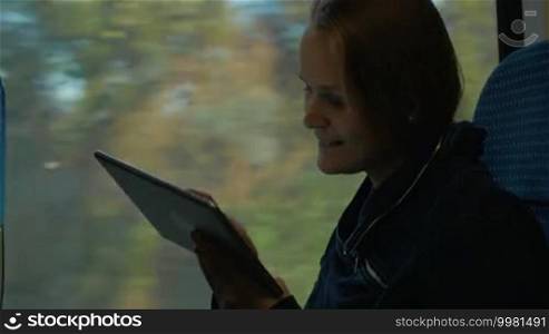 Young woman is staying in touch with friends with her tablet PC while traveling by train.