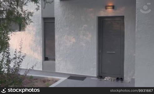 Young woman leaving home at sunset. She is putting on her shoes at the doorstep and walking away. Renting houses, villas, and hotels for holidays