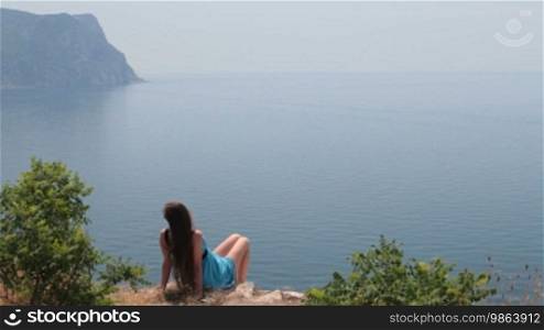 Young woman looks at the sea while sitting on the edge of a cliff, Black Sea, Balaklava, Crimea, Ukraine
