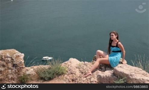 Young woman resting on the cliff near the Black Sea, Bay of Balaclava, Crimea. In the background, a pleasure boat sails.