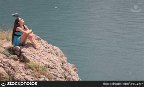 Young woman resting on the edge of a cliff by the sea in Balaklava, Crimea, Ukraine