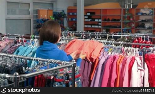 Young woman shopping for clothes in a clothing store, choosing children's jacket