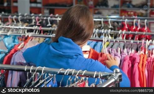 Young woman shopping for clothes in a clothing store, choosing children's wear