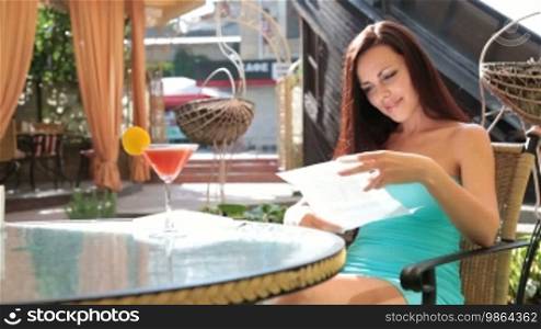 Young woman smiling received good news in a letter. She sits at a table in a cafe.