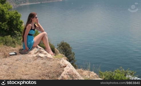 Young woman talking on a cell phone while sitting on top of a cliff
