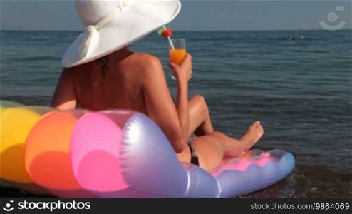 Young woman tanning on the beach with a cocktail in hand