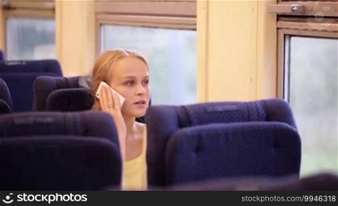 Young woman traveling by train and talking on the phone. After the call, she is looking out the window