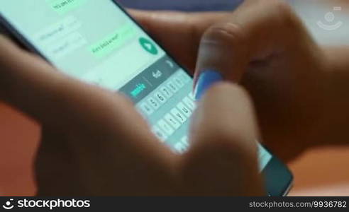 Young woman using smartphone while doing homework. Hispanic people and college education. Female student studying and texting with mobile telephone at home, typing text message on cell phone. Close-up