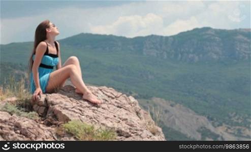 Young woman wearing blue dress relaxing on rocks