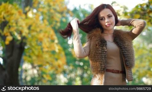 Young Woman Wearing Fur Vest in the Autumn Park, Looking At Camera
