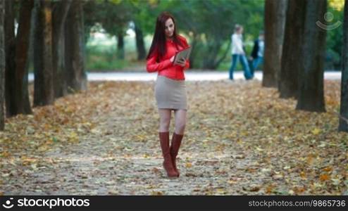 Young woman wearing red leather jacket using tablet computer in autumn park