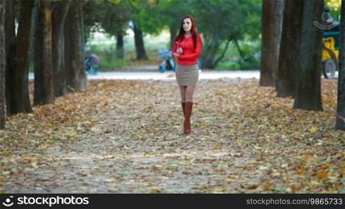 Young woman wearing red leather jacket with tablet computer in autumn park