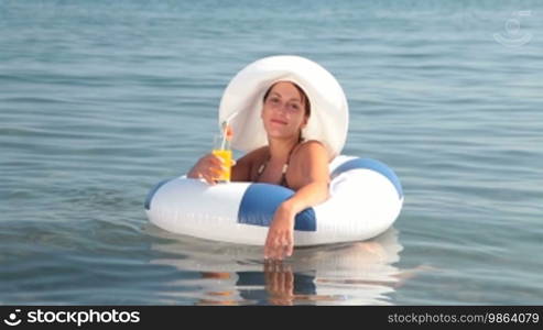 Young woman with cocktail in hand floating on innertube