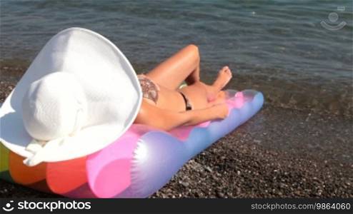 Young woman with white hat relaxing at the beach, rear view. She is sunbathing by the sea