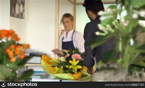 Young woman working as a florist giving receipt and credit card to customer after purchase. Dolly shot
