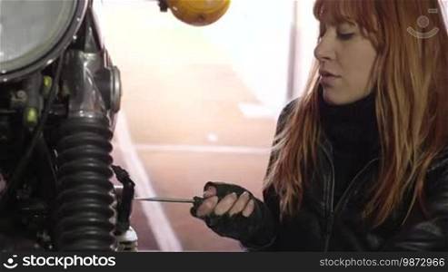 Young woman working as a mechanic in a garage, portrait of a girl smiling after repairing a motorbike with utensils, fixing the engine with tools. People, motorcycle, bike. 16 of 16