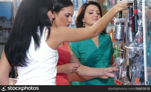 Young women shopping in cosmetics store, choosing hairbrush