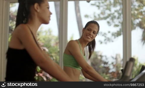 Young women talking and laughing while working out on exercise bicycles in wellness club