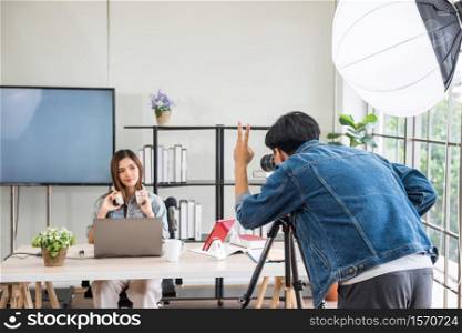 Video or professional digital camera man shoot or record live streaming of beautiful attractive Asian woman blogger podcaster with studio lighting. broadcasting for online journal or website content.