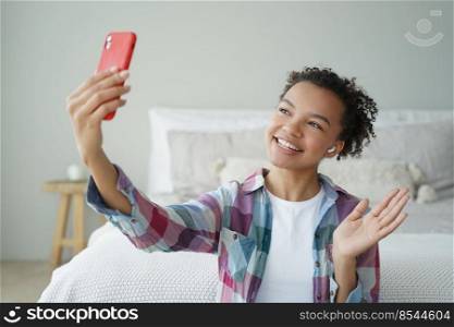 Video phone call. Curly african american woman is talking to friend on mobile phone. Young woman is speaking in front of camera and waving hand. Virtual communication concept. Teenage girl lifestyle.. Young woman speaking in front of camera and waving hand. Virtual communication concept.