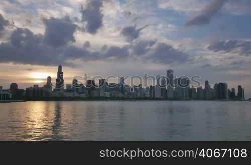 Video time lapse of Chicago downtown skyscrapers reflected on the Michigan lake from sunset clouds motion to night. Awesome Chicago city center skyline at night in the United States of America. Illuminated skyscrapers of Chicago in Spring twilight. Chicago sky in the evenig with the sun on the city sky.