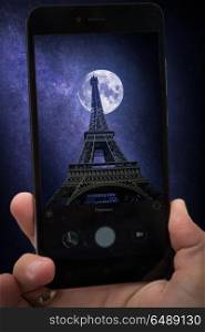 videobloger takes pictures on a smartphone. Eiffel Tower in Paris, France. The stars and the moon shine at night.. Eiffel Tower in Paris, France