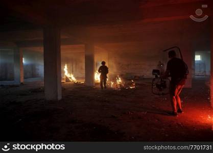 Videographer with Professional Movie Video Camera Gimbal Stabilizing Equipment Taking Action Shoot of Soldiers in Action in urban environment with fire effect