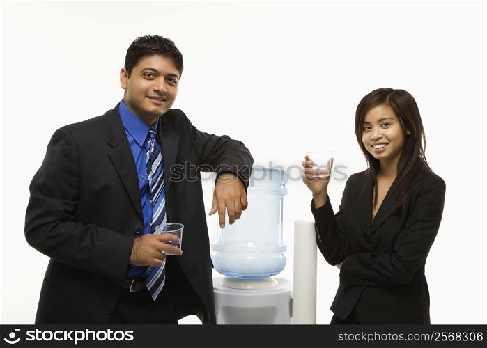 Vietnamese businesswoman and Indian standing at water cooler looking at viewer.