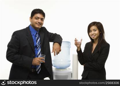 Vietnamese businesswoman and Indian standing at water cooler looking at viewer.