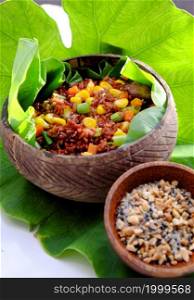 Vietnamese cuisine from red rice, delicious and nutrition rice dish for lunch, homemade food rich nutritious in coconut shell bowl with sesame salt on green leaf background