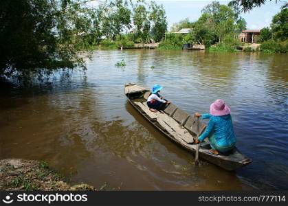Vietnamese woman transport little girl go to school by wooden boat, daughter and mother sit squat to cross river with bamboo along, landscape of Vietnam countryside at Mekong Delta on day