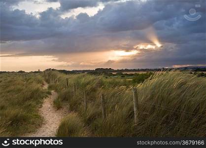 View across sand sunes to countryside with sunbeams through stormy clouds