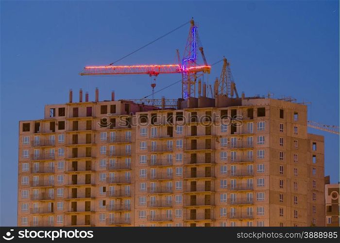View after sunset on the unfinished house with a crane. Construction of multi-storey building with a crane