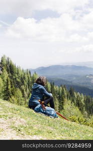 View at female hiker enjoying the mountain air sitting on a grass and resting