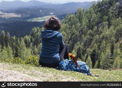 View at female hiker enjoying the mountain air sitting on a grass and resting