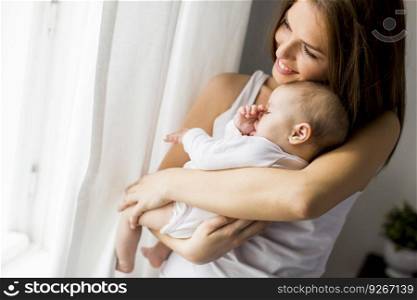 View at happy mother with newborn baby girl by window