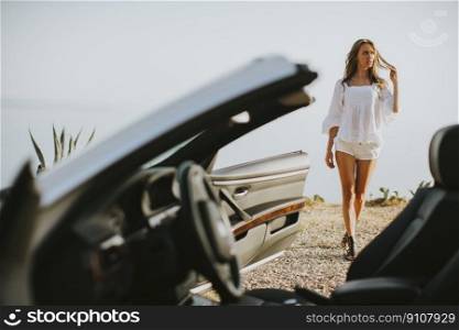 View at young attractive woman poses next to a  cabriolet at seaside