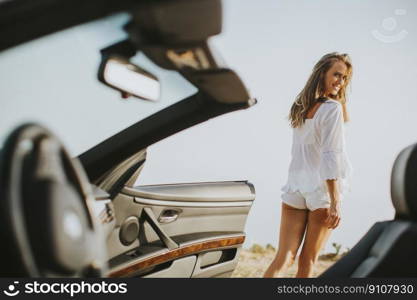 View at young attractive woman poses next to a  cabriolet at seaside