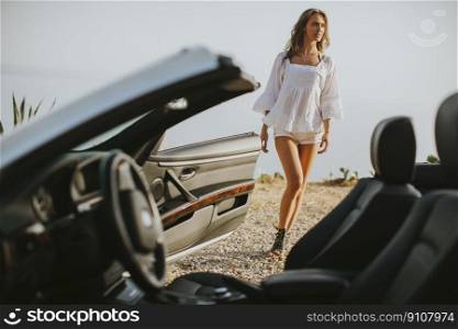 View at young attractive woman poses next to a  cabriolet at seaside