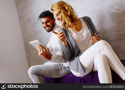 View at young couple with tablet and mobile phone on sofa