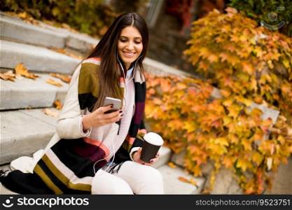 View at young woman sitting outside, drinking coffee to go and holding a mobile phone in hand
