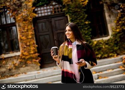 View at young woman standing outside, drinking coffee to go and holding a mobile phone in hand