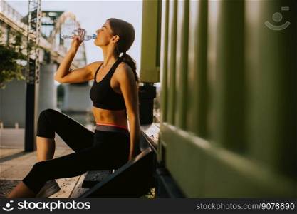 View at young woman taking a break during exercising outside and drinking water