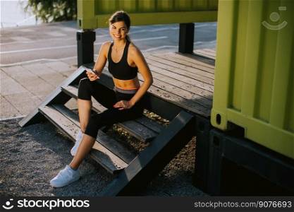 View at young woman taking a break during exercising outside and using mobile phone