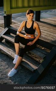 View at young woman taking a break during exercising outside and using mobile phone