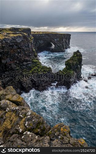 View during auto trip in West Iceland, Snaefellsnes peninsula, View Point near Svortuloft Lighthouse. Spectacular black volcanic rocky ocean coast with cave arch and towers.