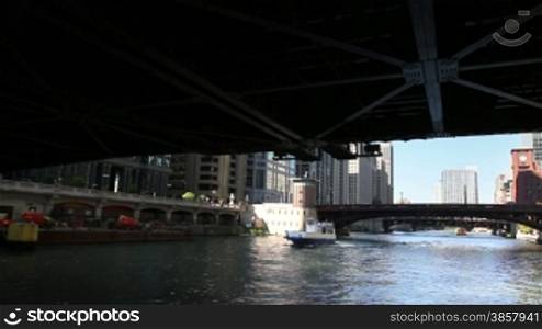 View from a boat as it passes underneath a bridge and passes another boat on the Chicago River in the middle of downtown Chicago.