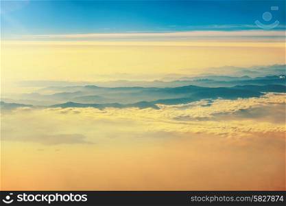 View from a plane to orange sunset on the sky with sunrays. Fluffy clouds background