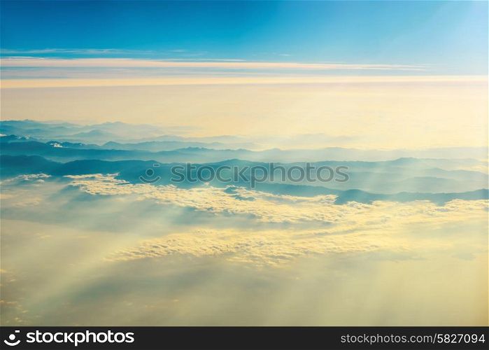 View from a plane to sunset on the sky with sunrays. Fluffy clouds background