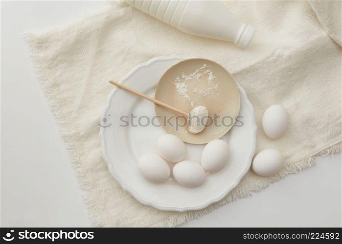 View from above of eggs and spoon of flour on white cloth. Cooking concept. Raw eggs and spoon of flour